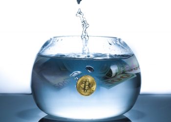 A bitcoin coin and $100 currency in a bowl being filled with water
