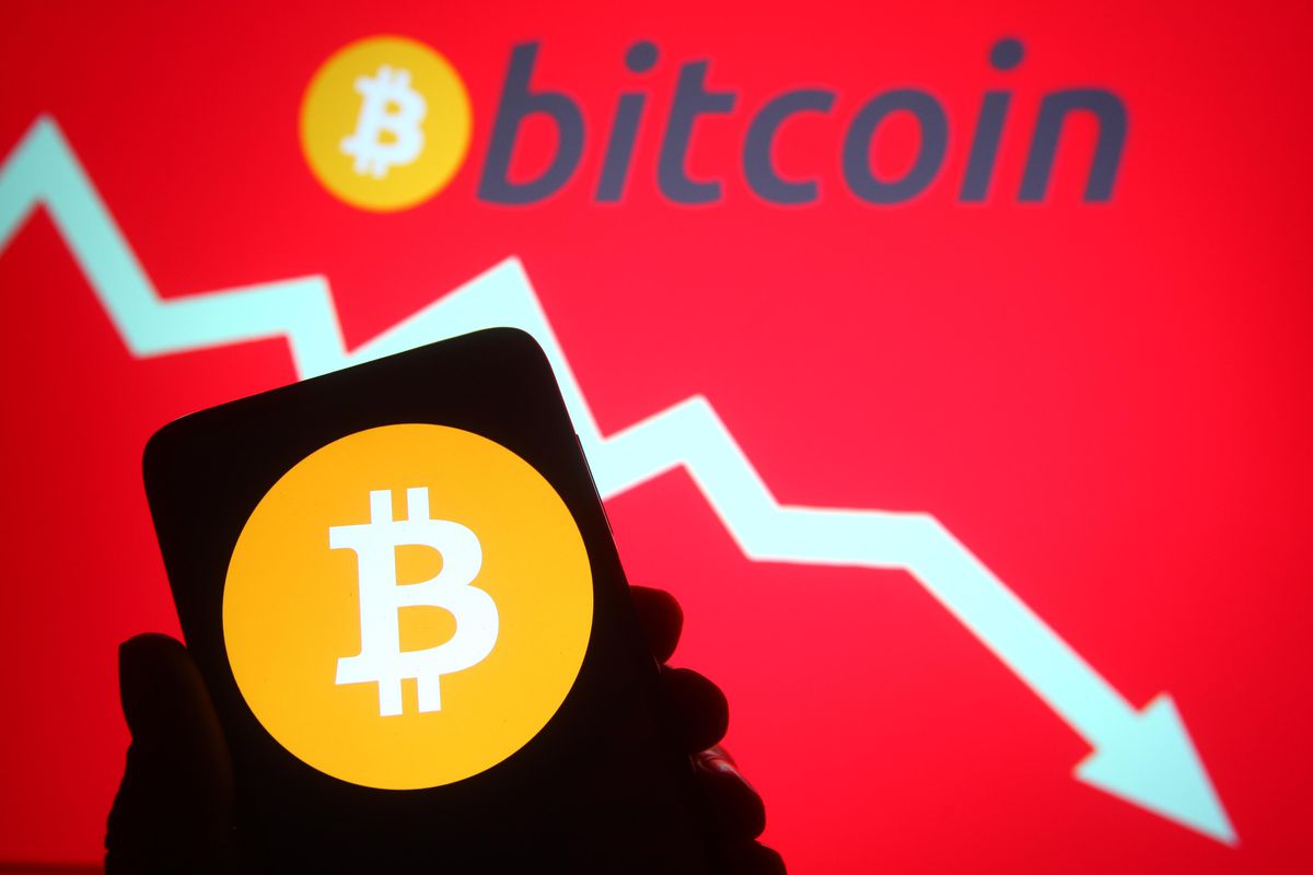 A hand holding up a phone with bitcoin on it. A white arrow points downward on a red background