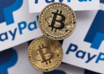 Two bitcoins on top of papers with PayPal symbol on them, representing payment methods using blockchain