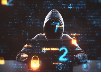 Picture of an anonymous hacker in front of a computer with computer code around them