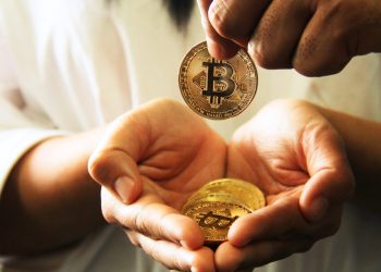 Picture of a hand holding Bitcoins, with another hand dropping a bitcoin in it