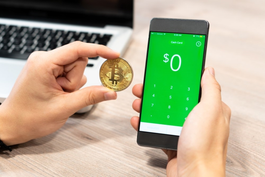 Picture of hand holding a bitcoin with Square's Cash App's buy bitcoin page on a mobile phone