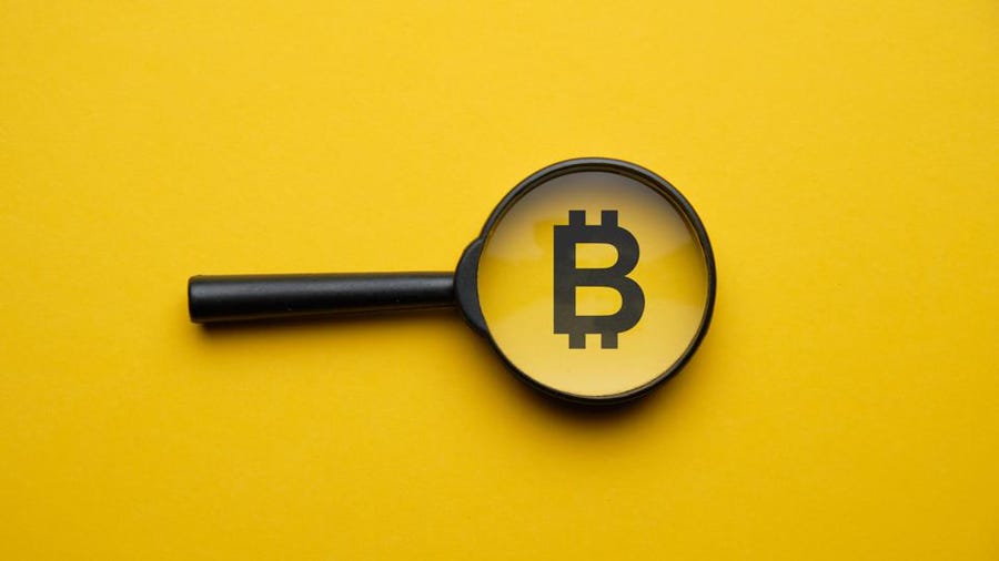 Picture of a bitcoin logo in the middle of a magnifying glass, with a yellow background