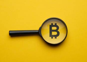 Picture of a bitcoin logo in the middle of a magnifying glass, with a yellow background