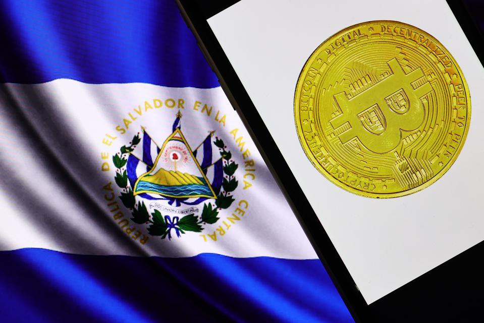 Picture of El Salvador flag with a mobile phone showing a bitcoin next to it
