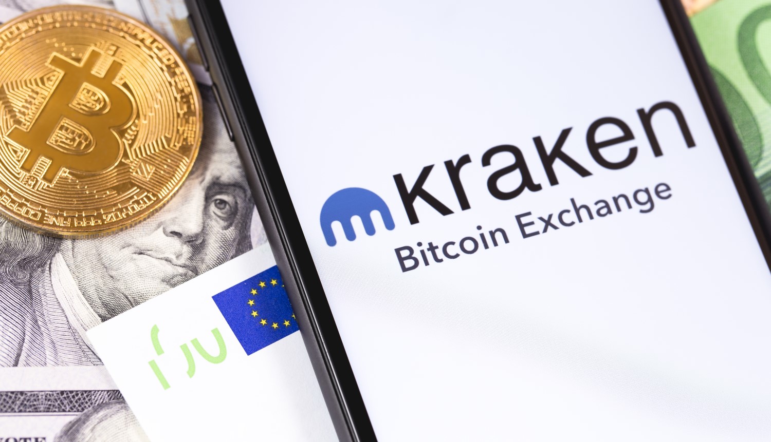 Picture of a gold bitcoin next to a smart phone with the Kraken app open on it