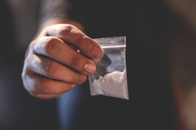 Picture of a hand holding a small bag of white powder depicting cocaine NFT