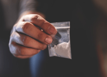 Picture of a hand holding a small bag of white powder depicting cocaine NFT