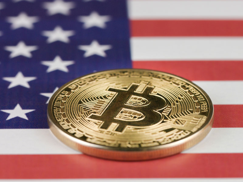 Picture of a bitcoin laying atop a U.S. flag