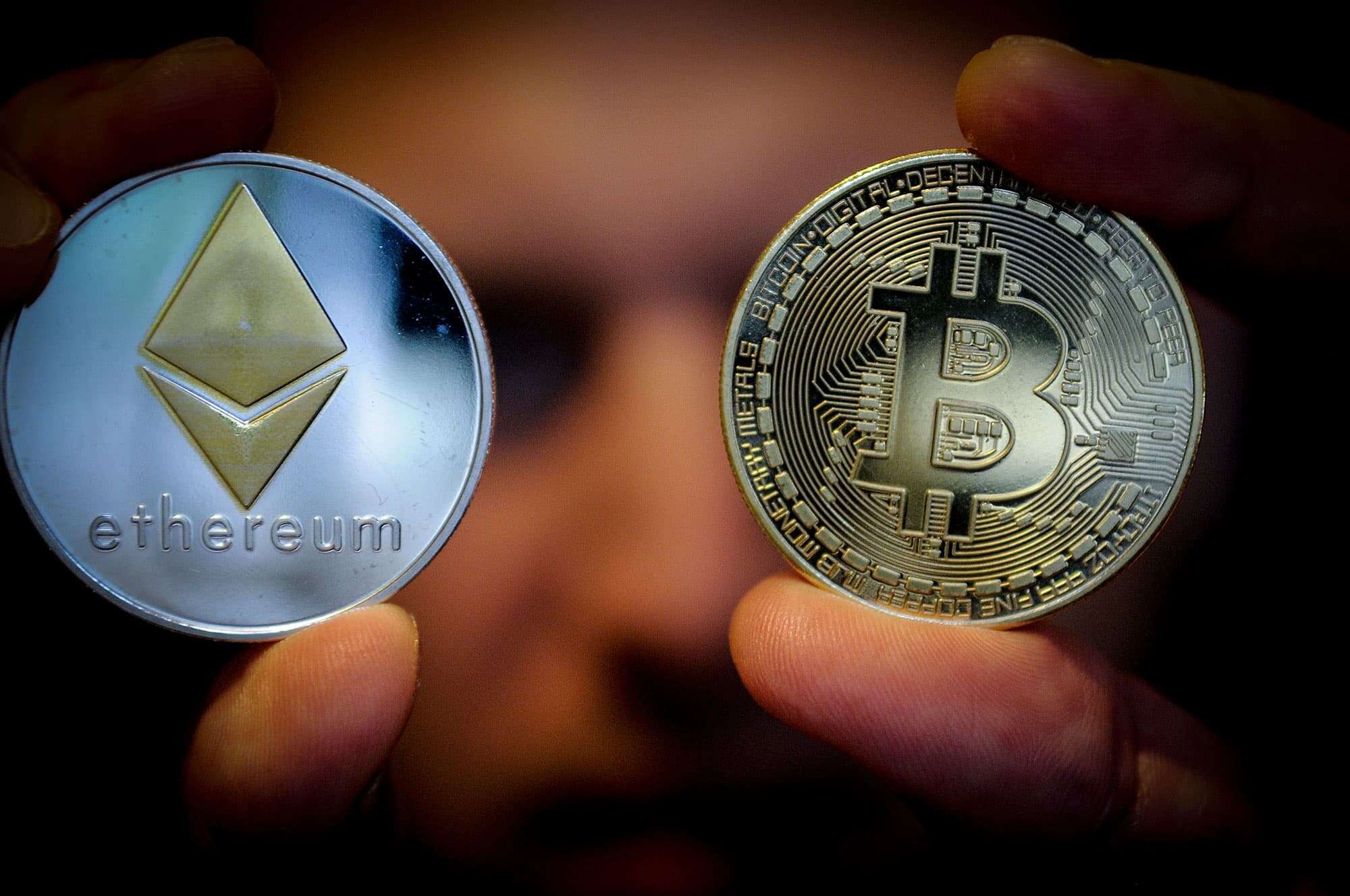 Picture of two hands holding a bitcoin and an ethereum coin