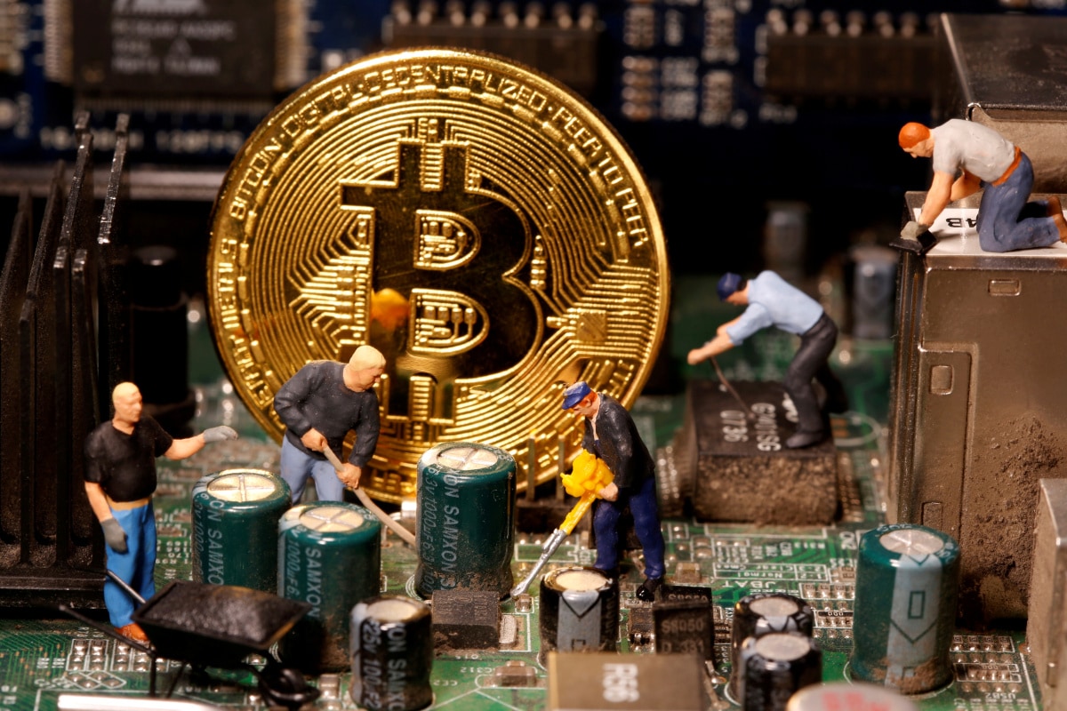 Picture of a gold bitcoin on a circuit board with figurine miners around it
