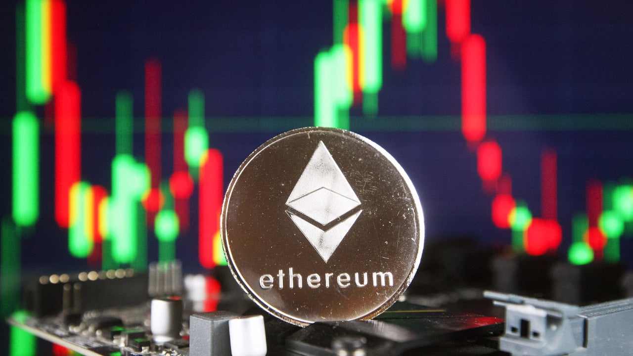 Picture of a silver ETH coin in front of a green and red candlestick chart