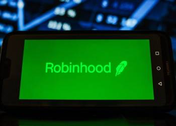 Picture of Robinhood logo on a mobile phone in front of a market chart