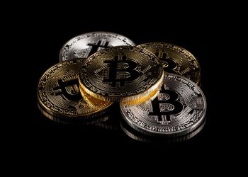 Picture of one bitcoin laying on top four bitcoins