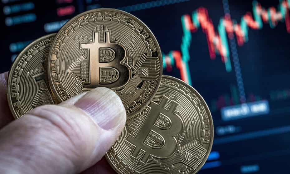 Hand holding three bitcoins in front of a market chart