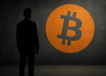 นักธุรกิจเงายืนต่อหน้าโลโก้ Bitcoin บนกำแพงคอนกรีต