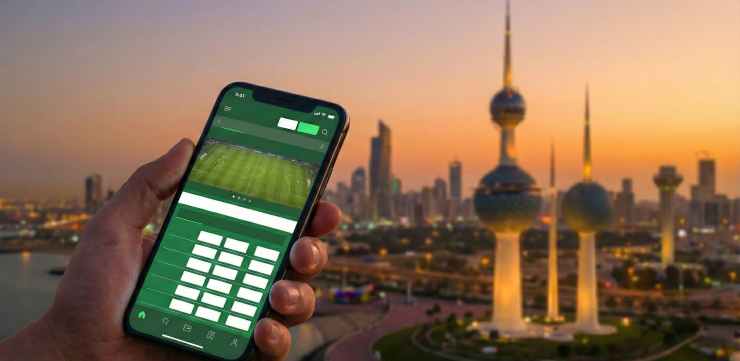 A hand holding a phone with a betting app open with Kuwait in the background