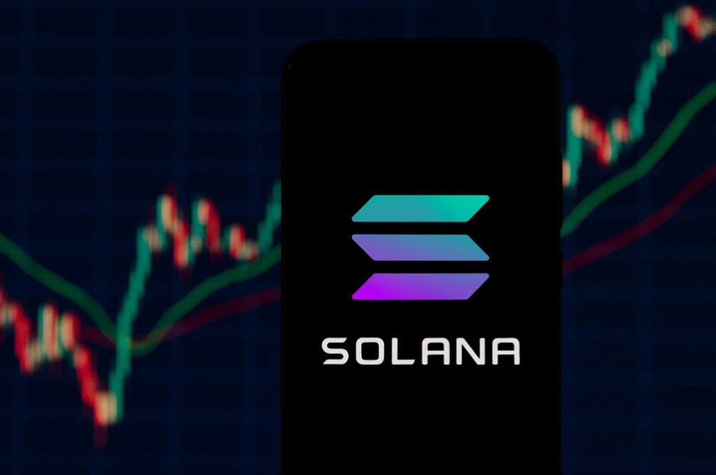 携帯電話に表示されたSolanaのロゴと背景にチャート
