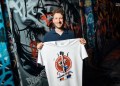Martin Masser, ChangeNOW’s Director of Strategic Partnerships, holds a branded T-shirt in a graffiti-covered London passage.